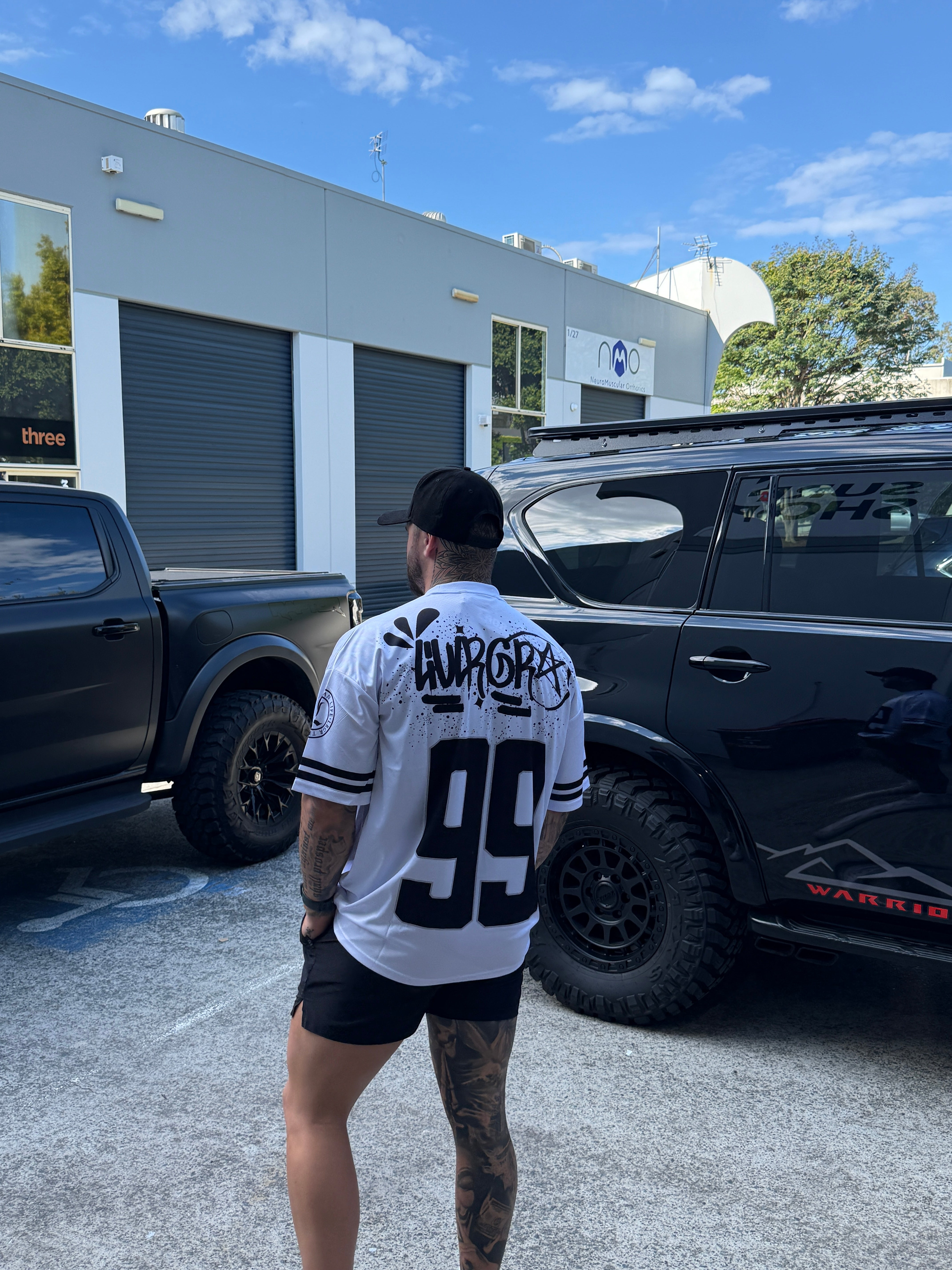 Person standing next to a black truck with a building and blue sky in the background