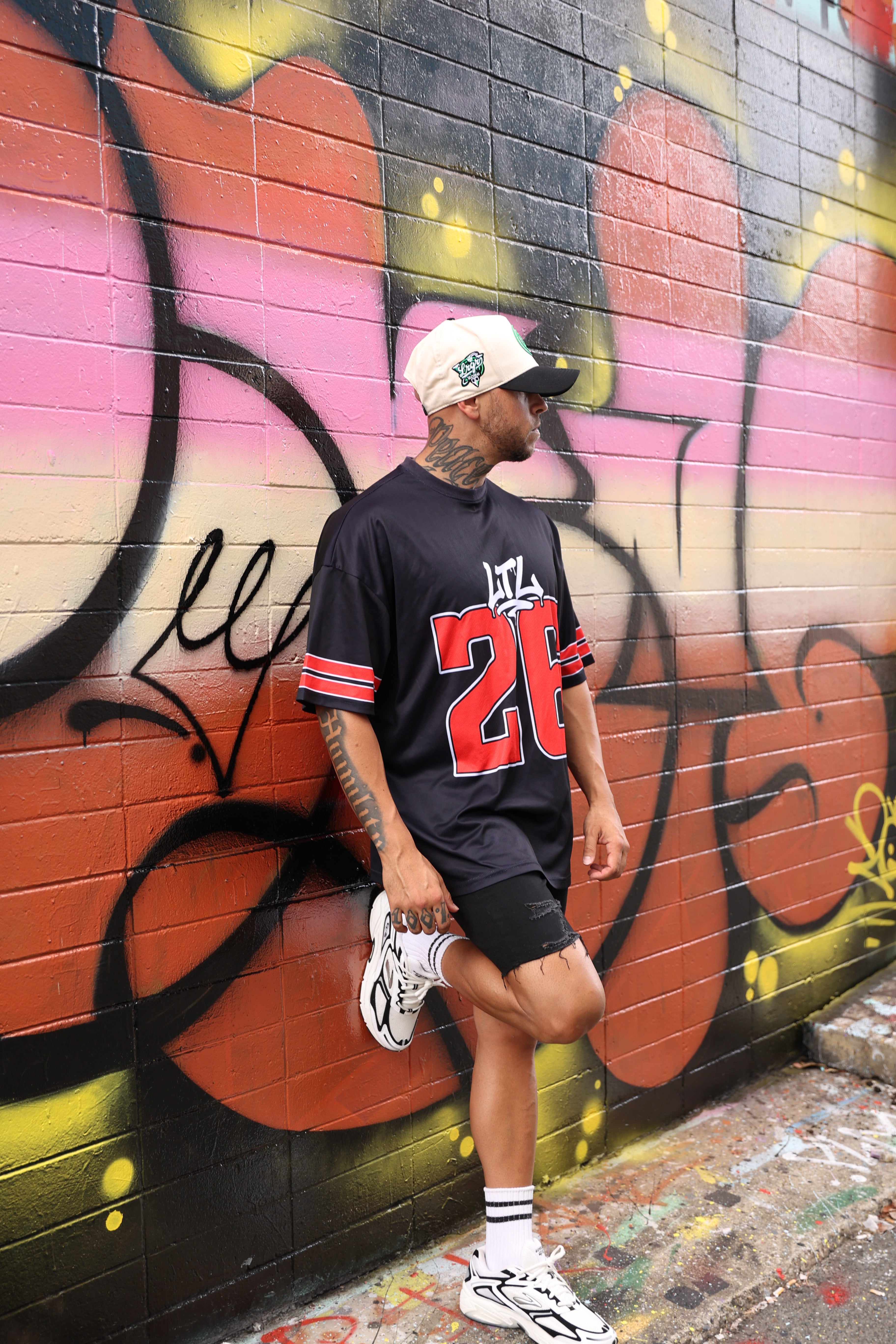 Person wearing a LRGR black oversized tee with red number 12 design, standing in front of colorful graffiti wall.