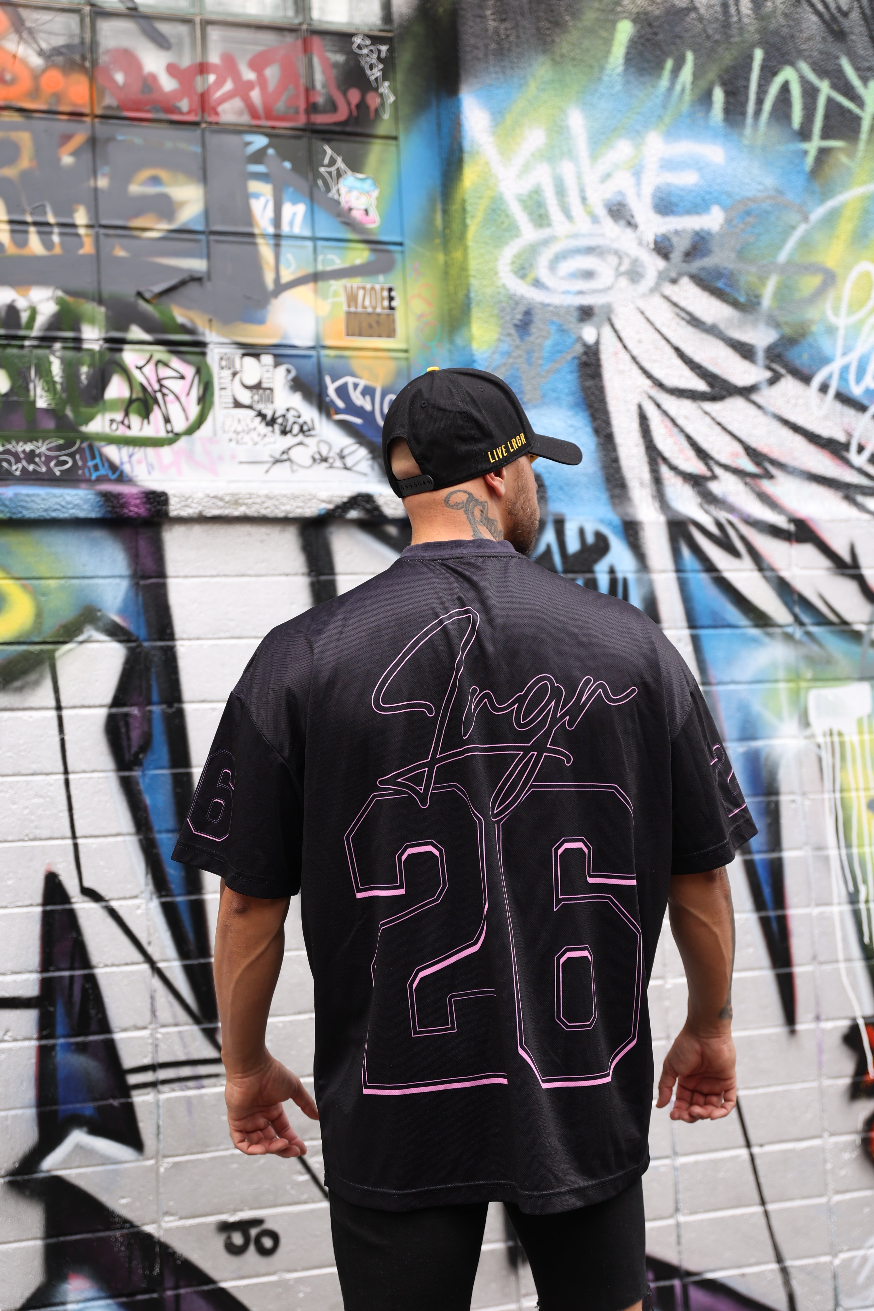 Person wearing a LRGR black t-shirt with pink designs in front of a colorful graffiti wall.