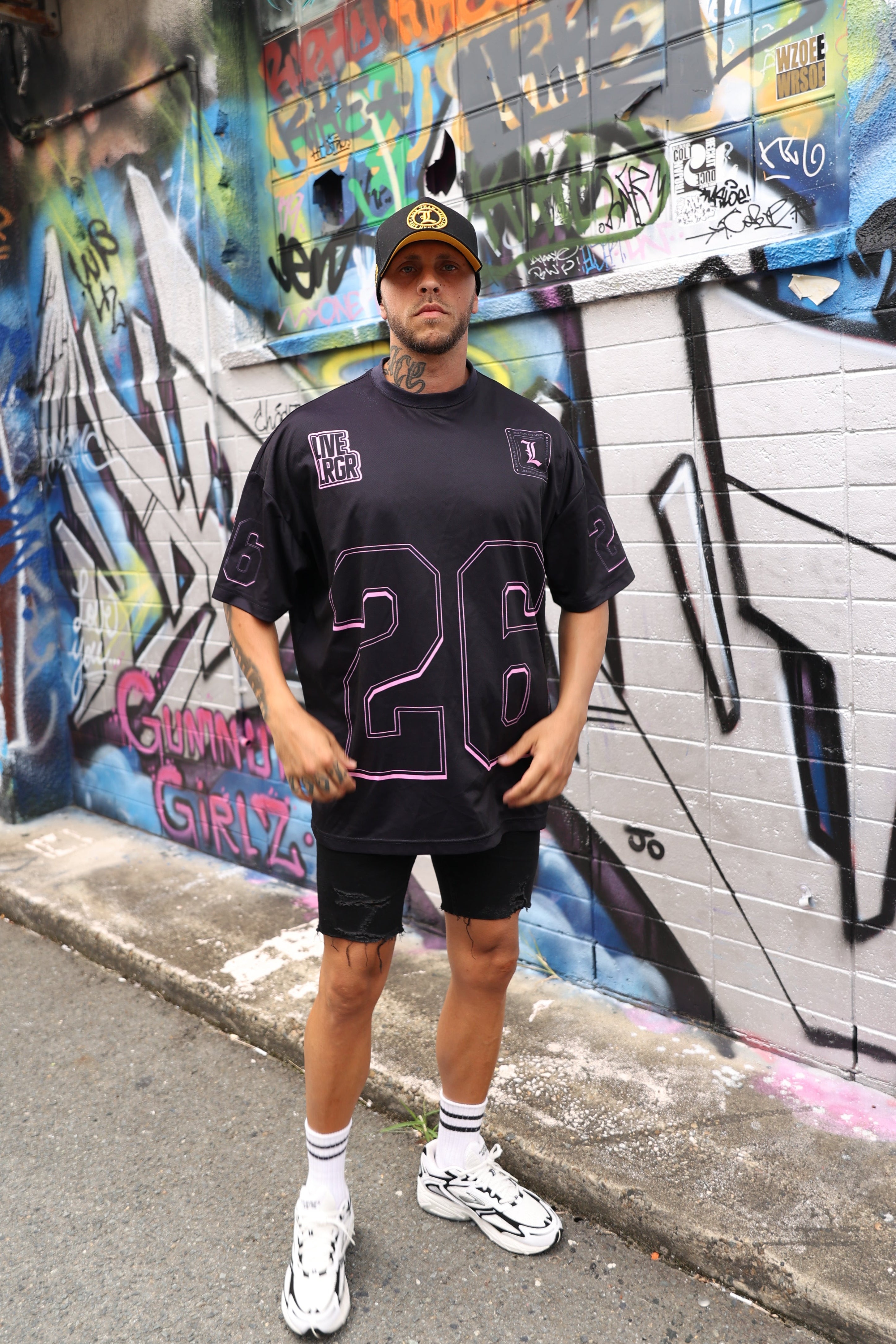 Person wearing a LRGR black t-shirt with a number design, standing on a graffiti-covered street.