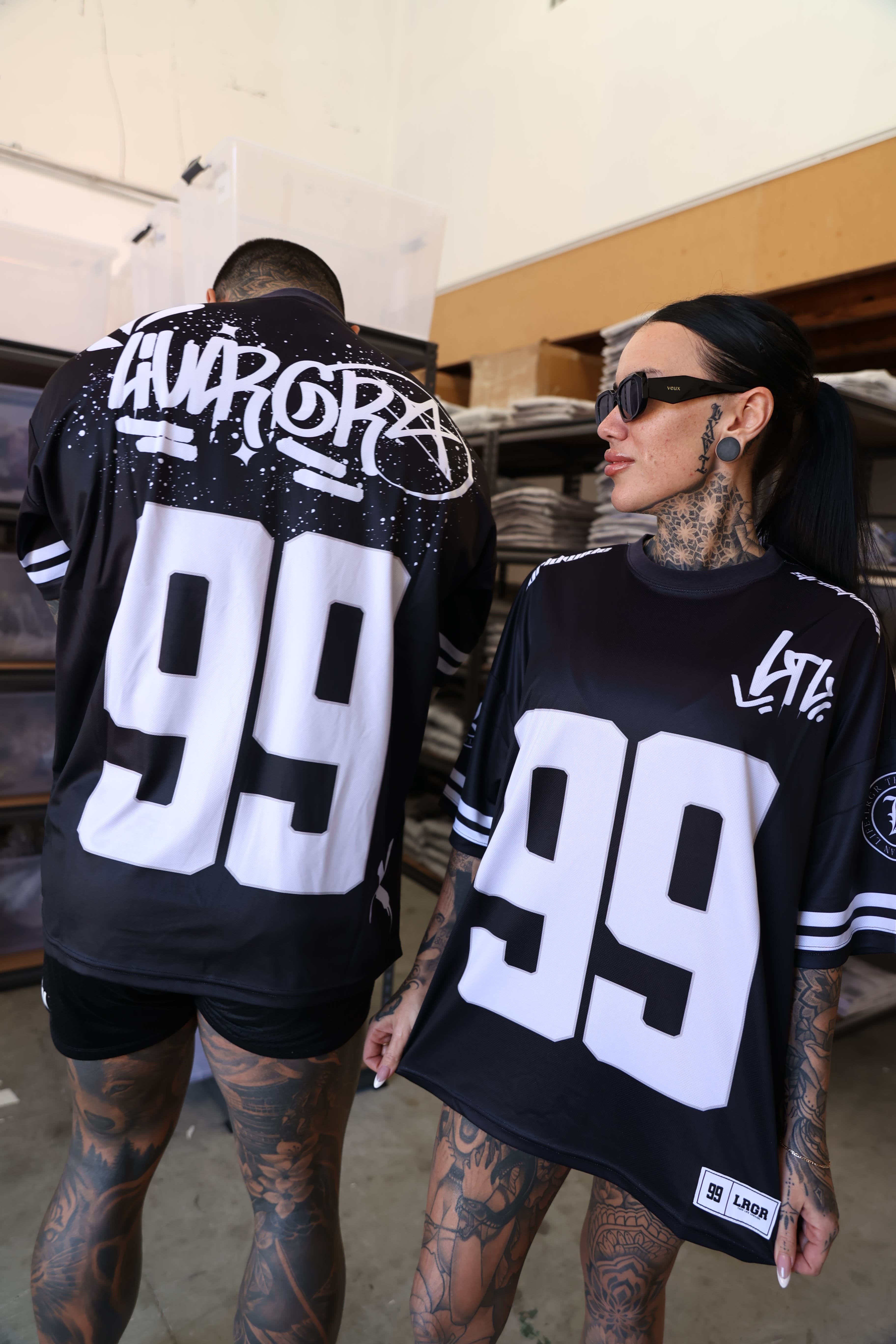 Two people wearing black jerseys with white numbers and text, sitting on a bench.