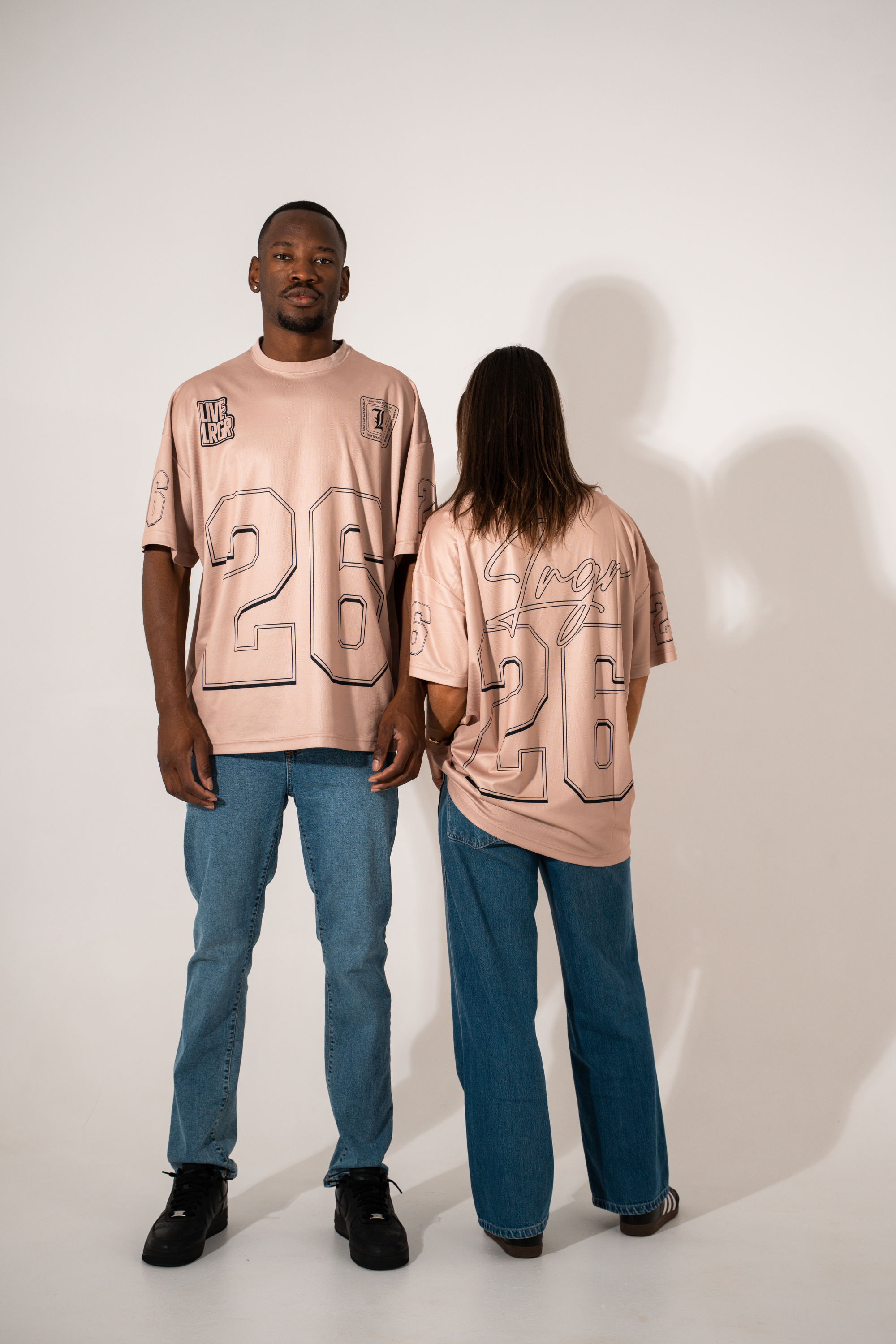 Two people wearing matching pink t-shirts with numbers on a plain background
