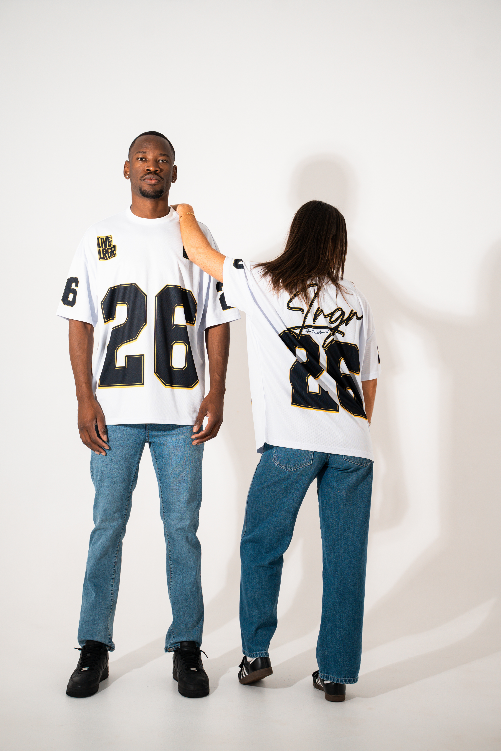 Two people wearing matching white jerseys with black numbers on a plain background