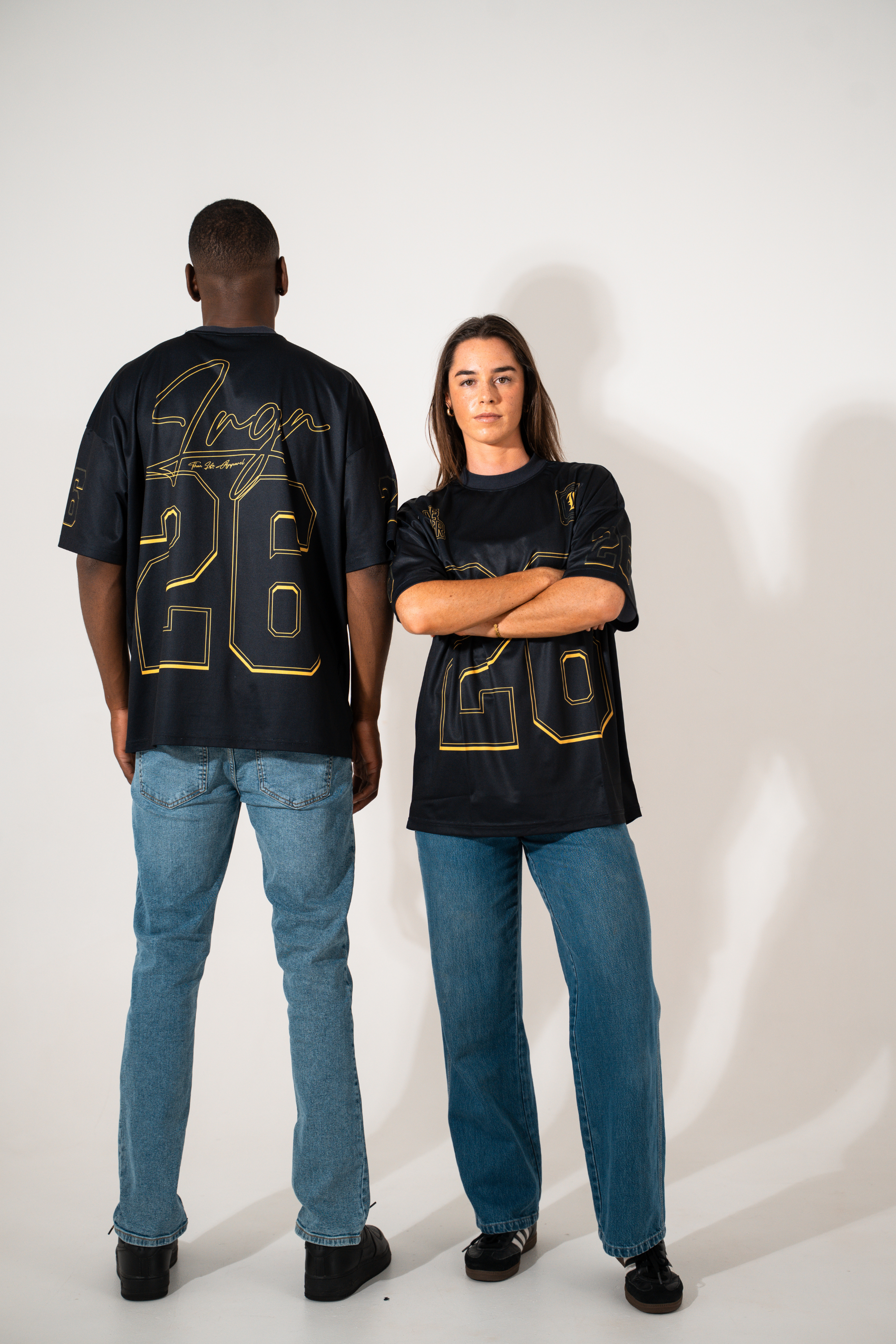 Two people wearing black t-shirts with gold text and numbers on a white background