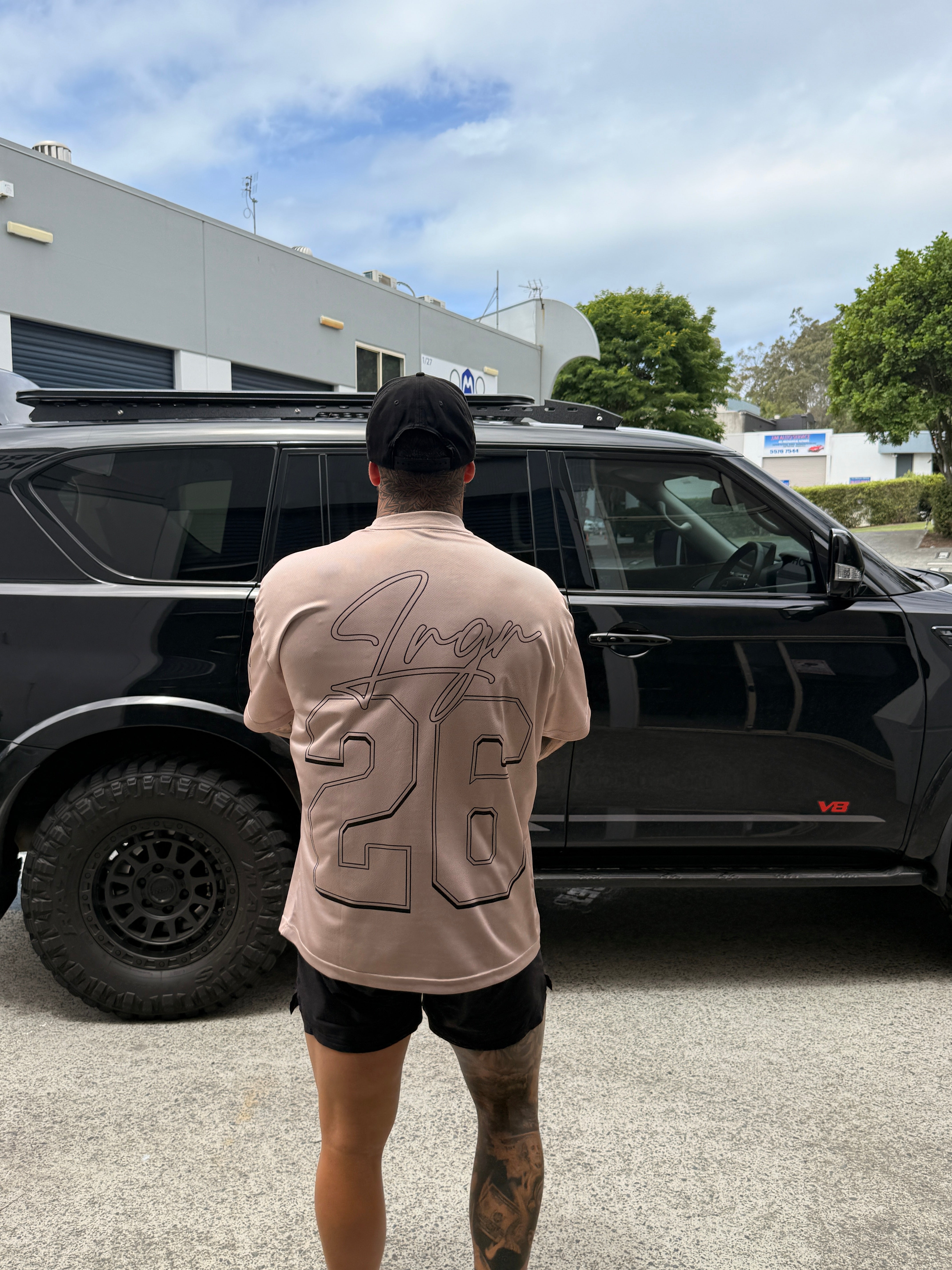 Person wearing a LRGR beige t-shirt with a logo, standing next to a black SUV on a street.