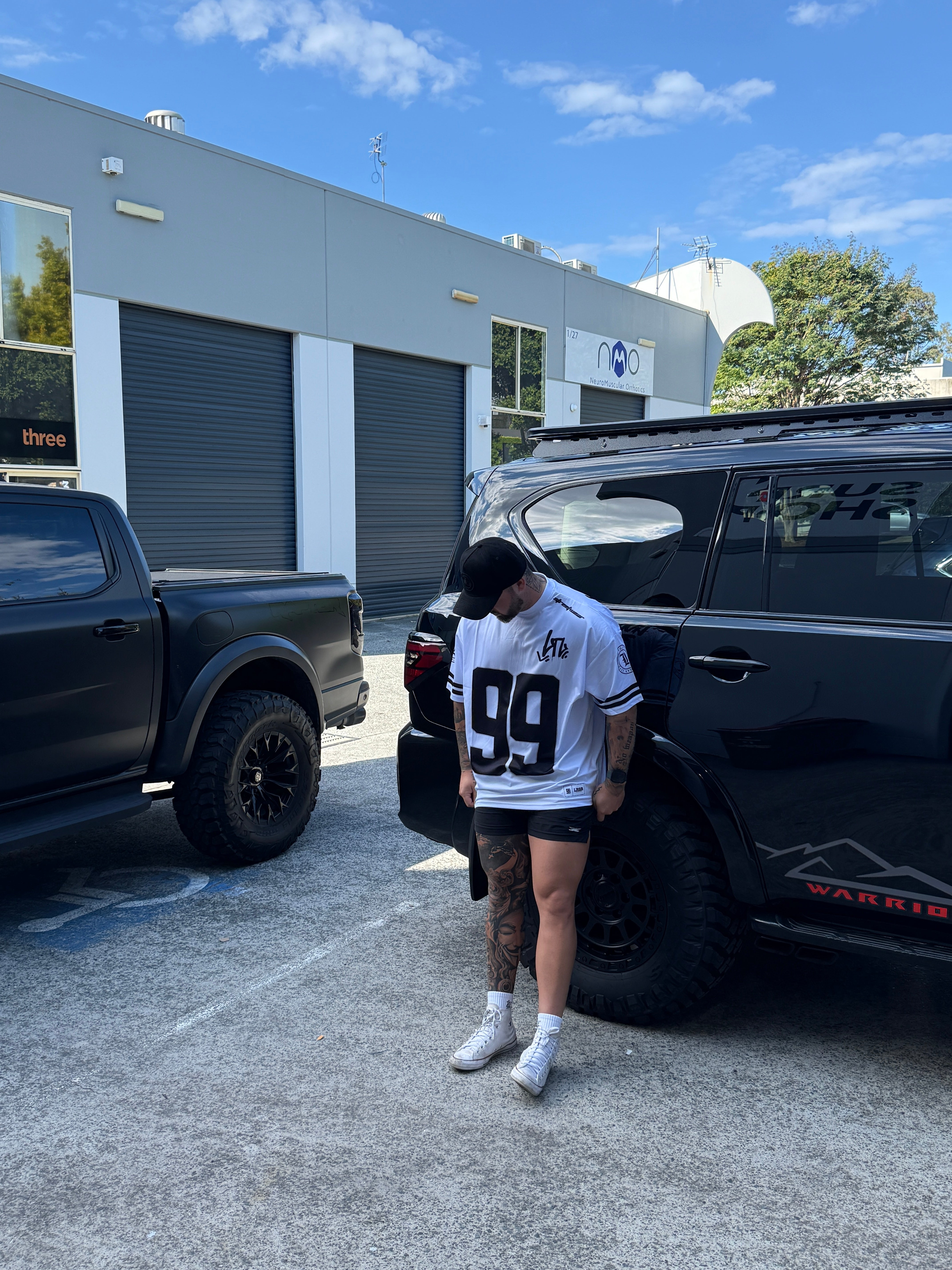 Two people standing next to a black truck with a building and blue sky in the background