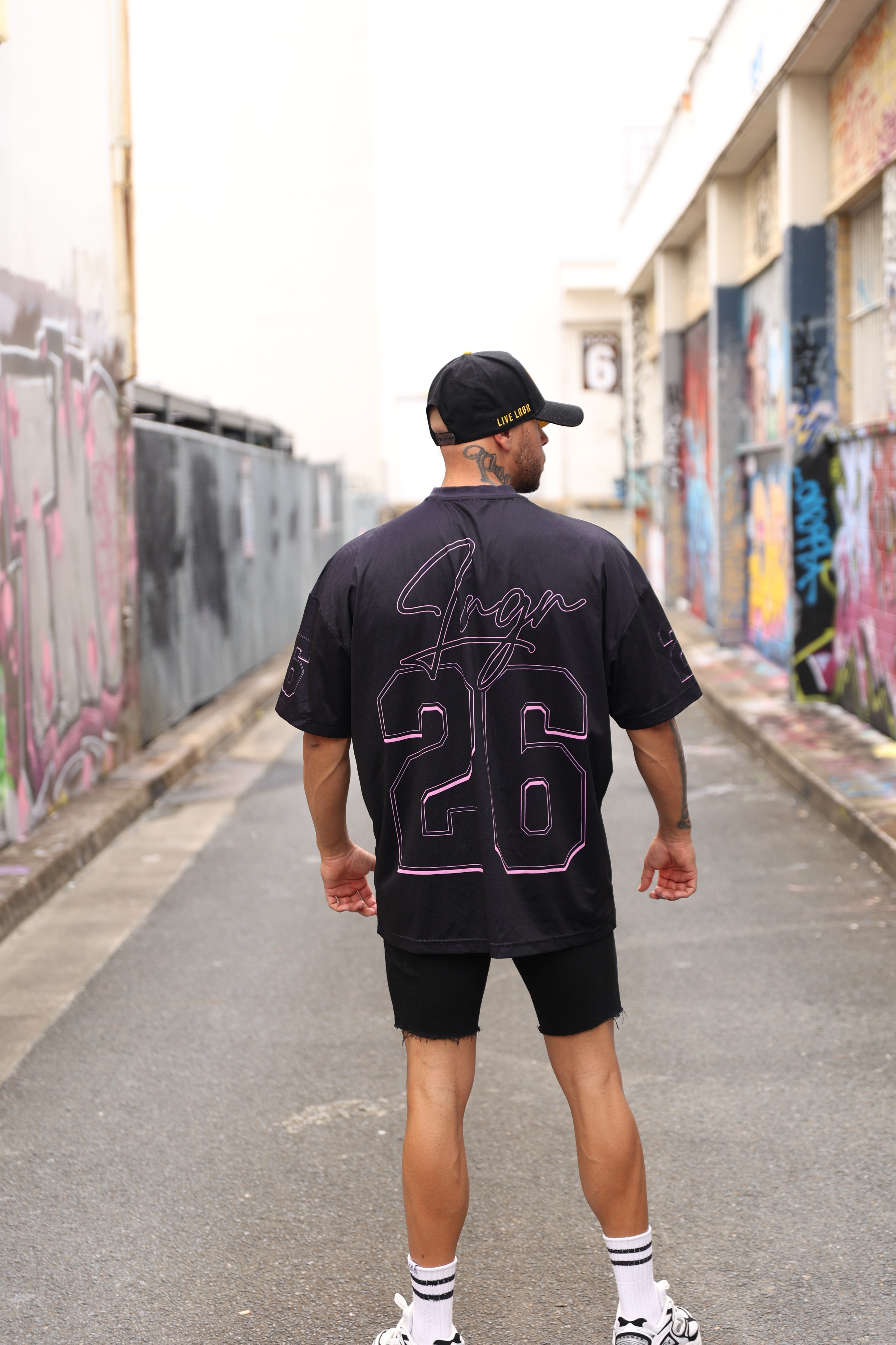 Person wearing a LRGR black t-shirt with pink text and graphics, standing on a street.