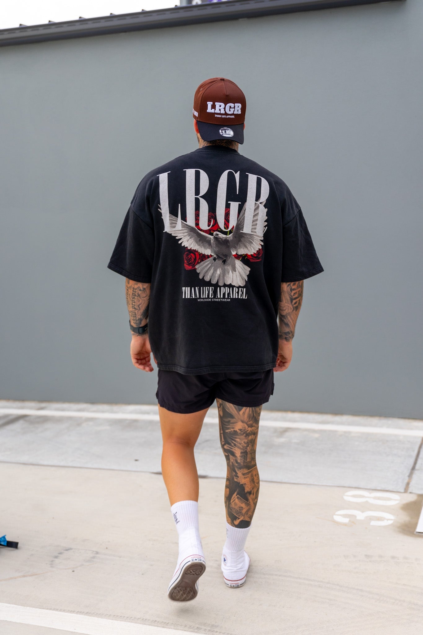Person wearing a black t-shirt with a logo and text, standing against a concrete wall.