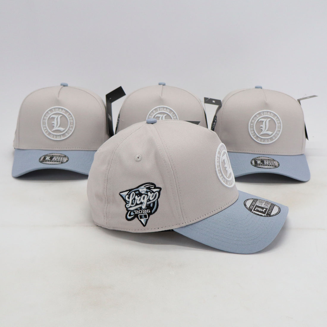 Four gray and light blue baseball caps with logos on a white background