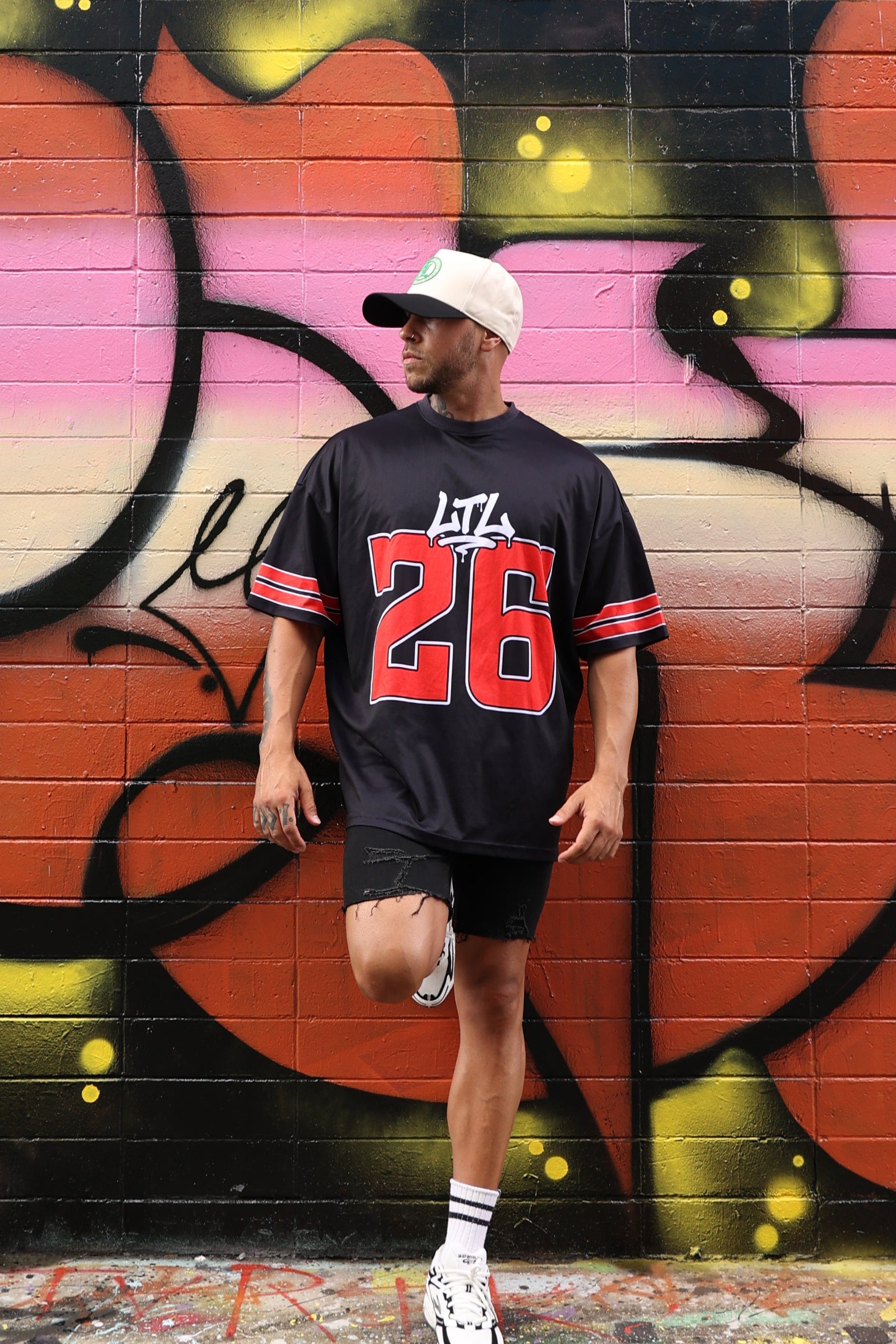 Person standing in front of a colorful mural with graffiti-style text on a wall.