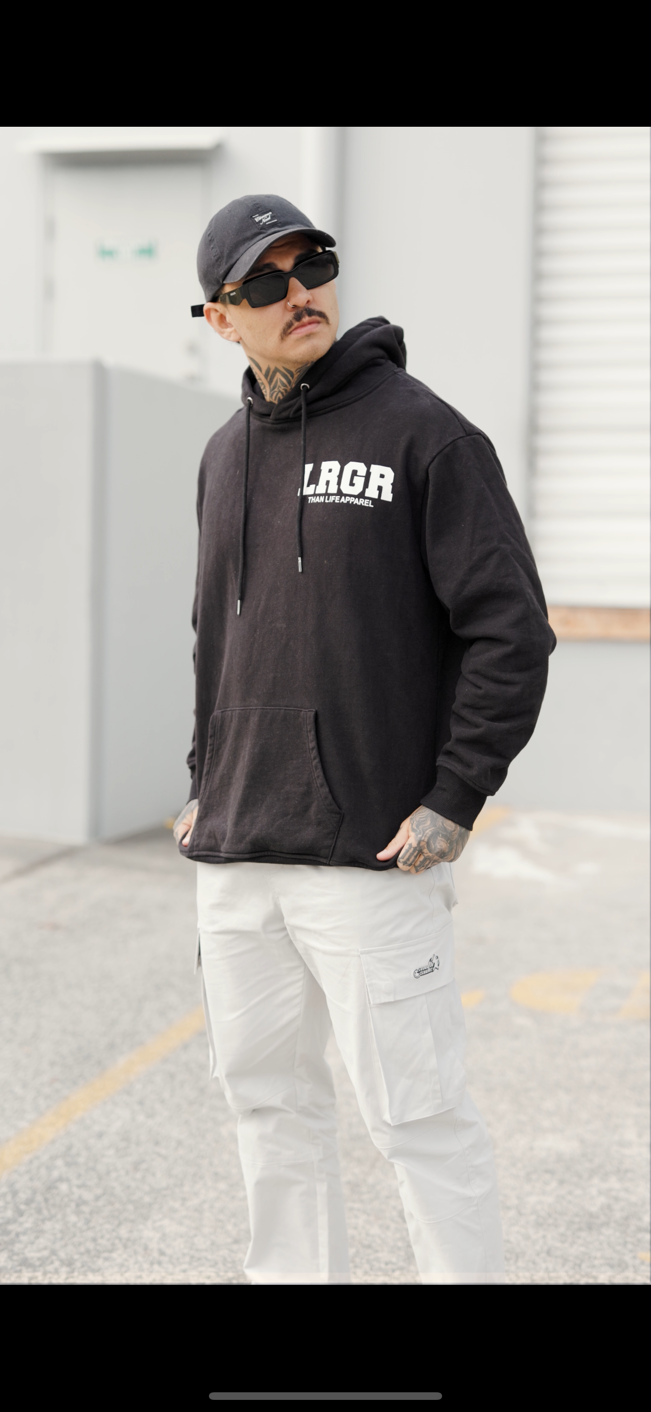 Person wearing a black hoodie with 'LRGR' branding on steps against a geometric wall.