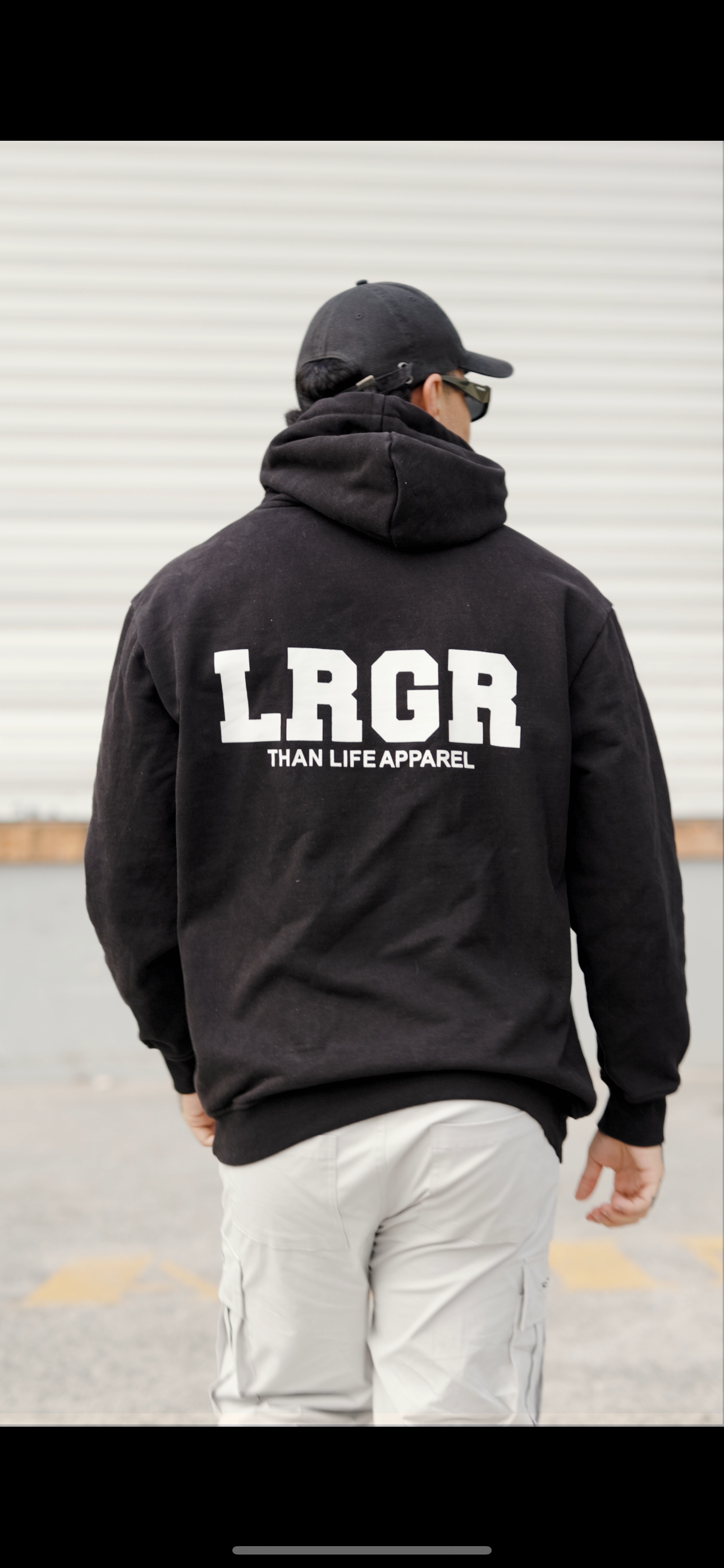 Person wearing a black hoodie with 'LRGR' branding on steps against a geometric wall.