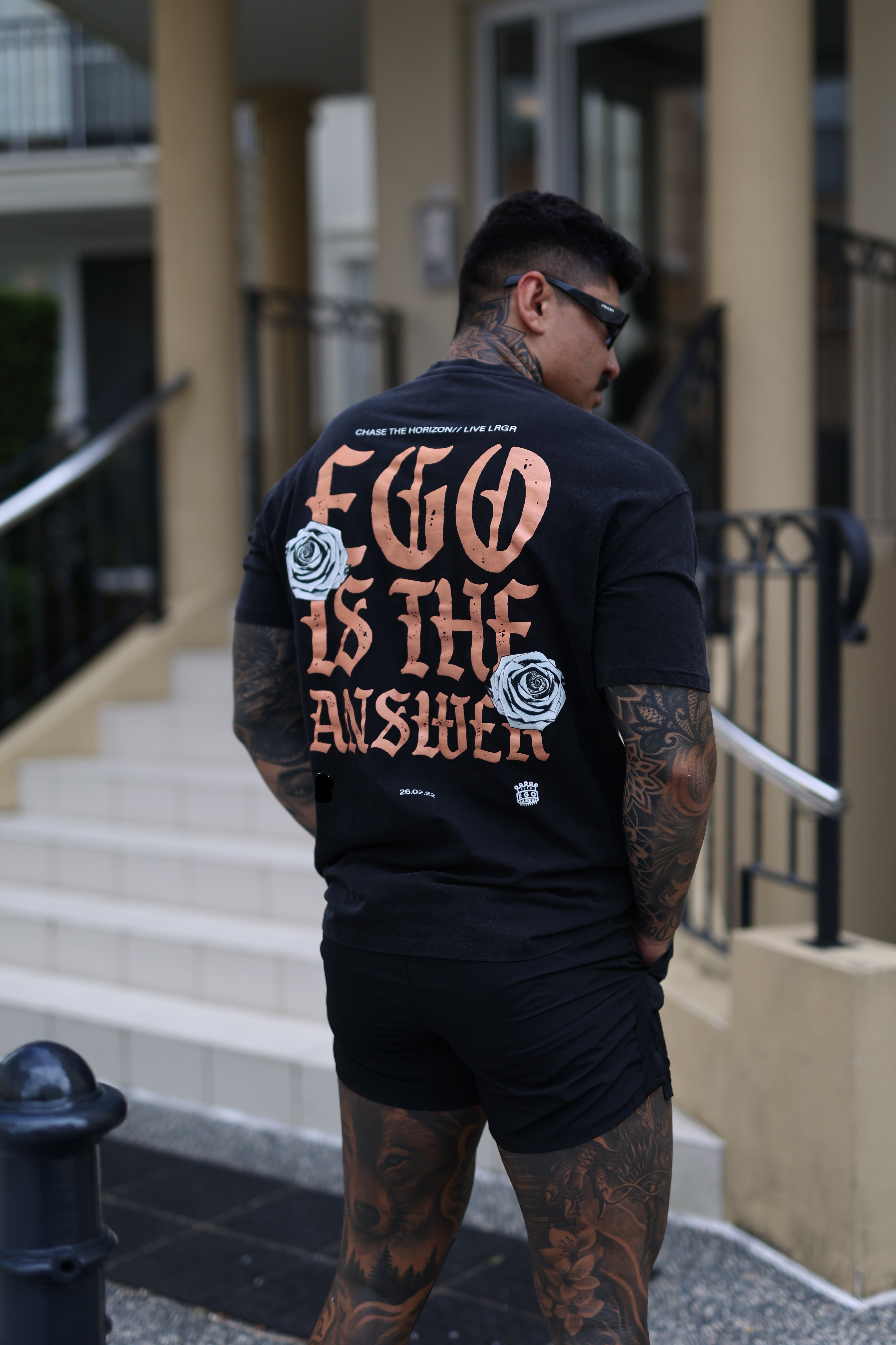 Person wearing a black hoodie with text and roses, standing on a street.