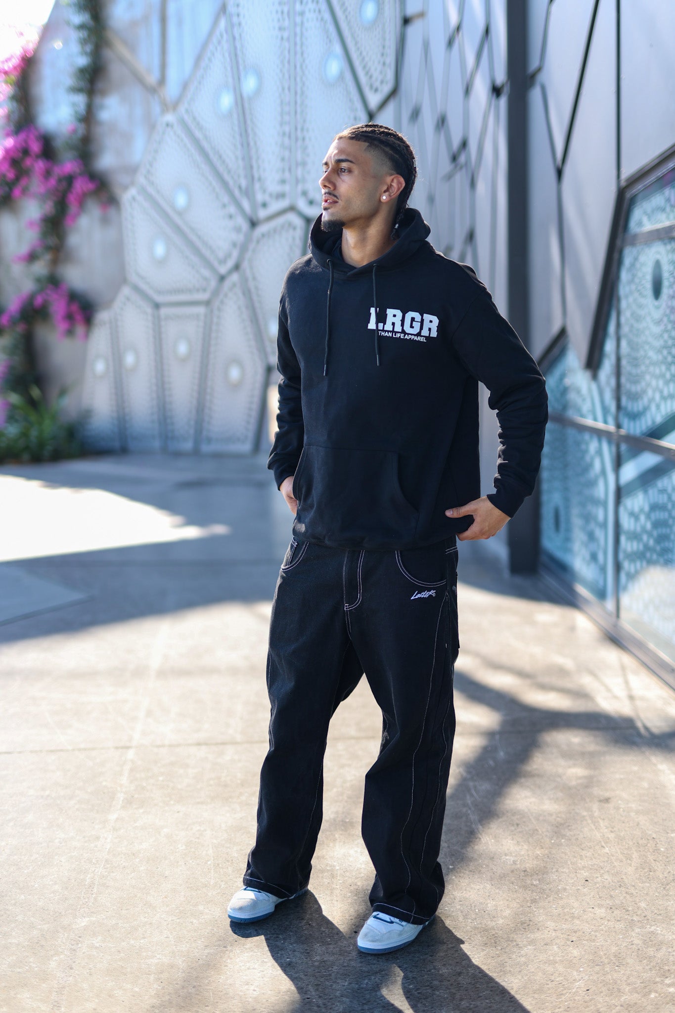 Person wearing a black hoodie with 'LRGR' branding on steps against a geometric wall.