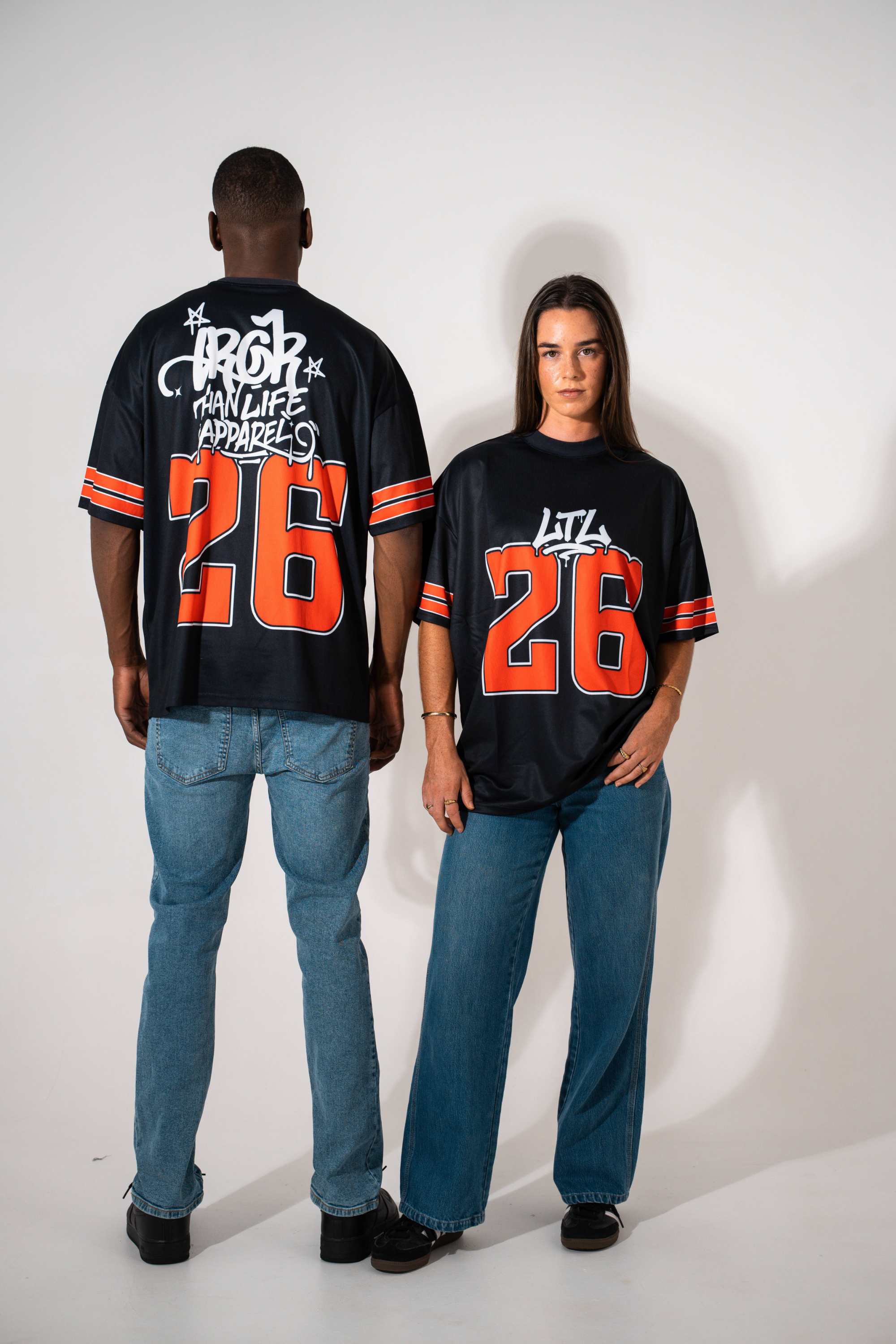 Two people wearing matching black jerseys with orange numbers on a white background