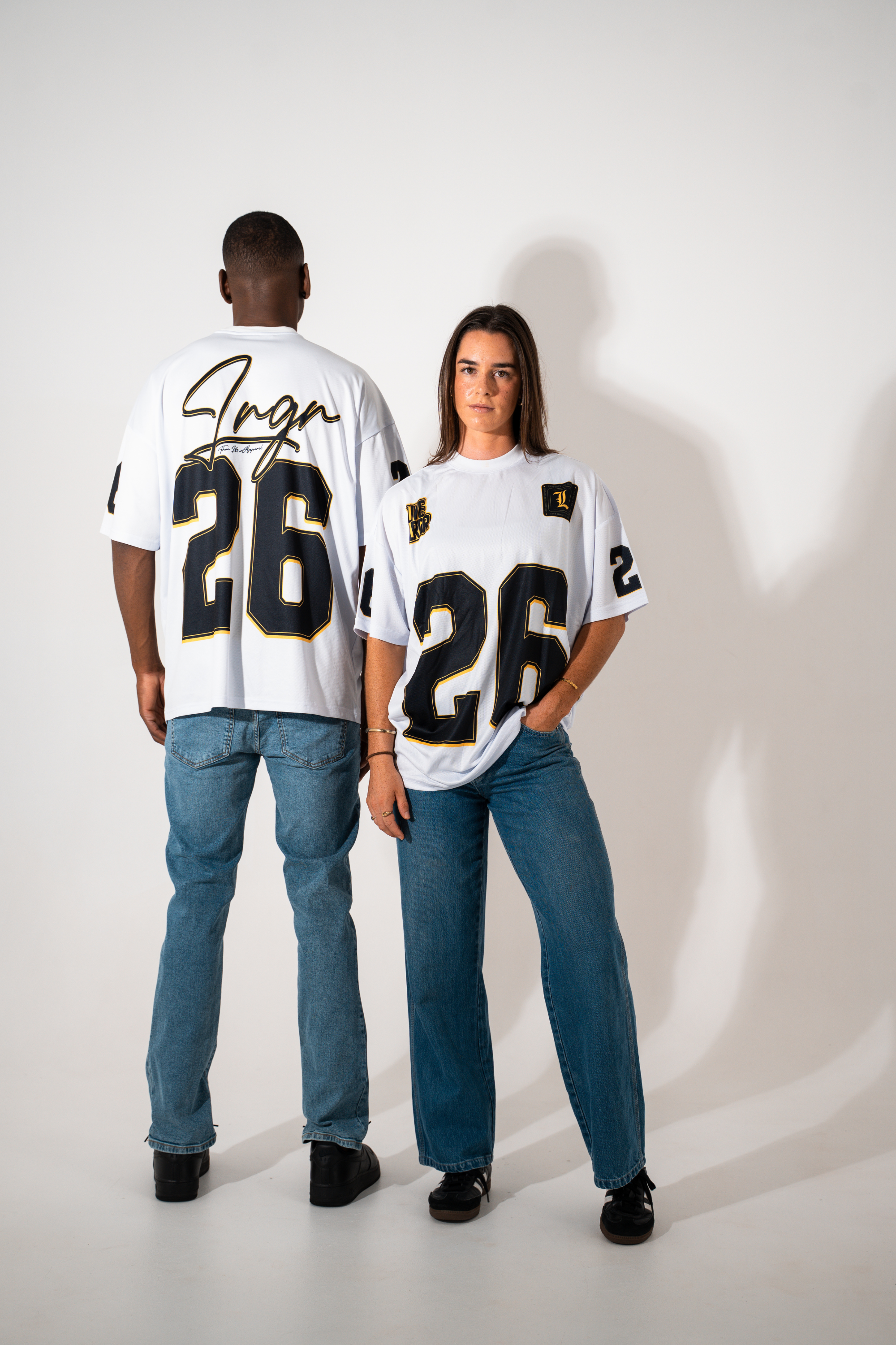 Two people wearing matching jerseys with the number 26 on a plain background