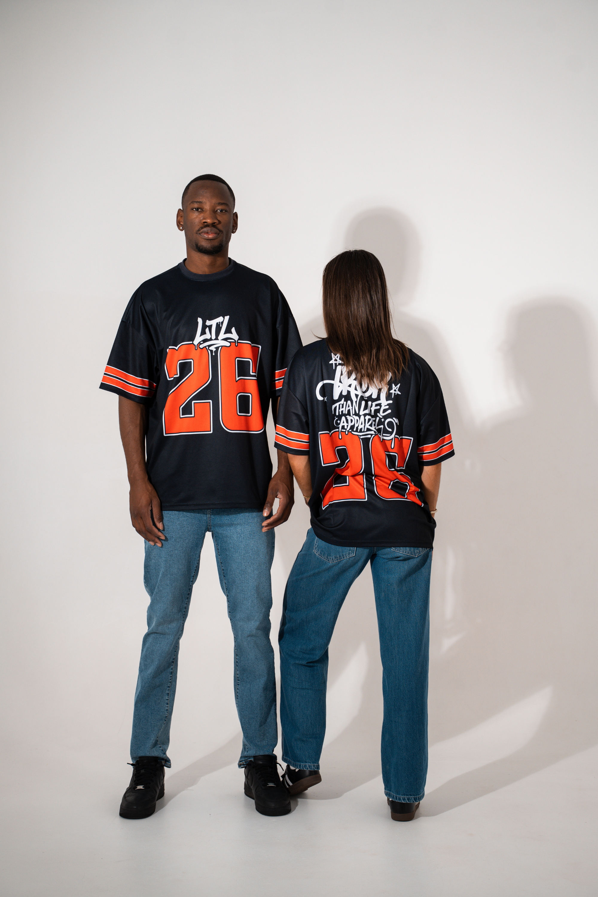 Two people wearing matching black jerseys with orange numbers on a white background